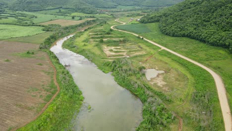 Ackerland-Und-Berge-In-Muak-Klek,-Thailand,-Eine-Rückwärtige-Luftaufnahme,-Die-Diese-Landwirtschaftsstraße-Auf-Der-Rechten-Und-Den-Schlammigen-Fließenden-Fluss-In-Der-Mitte-Zeigt