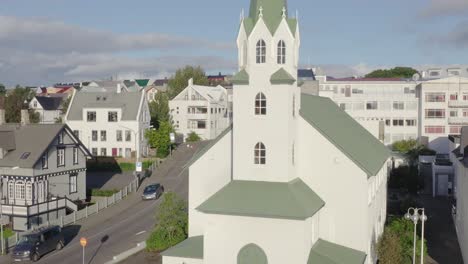 Rising-beside-idyllic-church-revealing-traditional-Iceland-houses-in-capital,-aerial