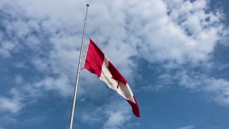 Canadian-flag-at-half-mast-waving-on-pole-with-cloudy-blue-sky-during-mourning