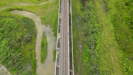 An-aerial-footage-revealing-a-railway,-birds-flying,-grassland-on-the-right,-a-canal-of-water-on-the-left,-Saraburi,-Thailand