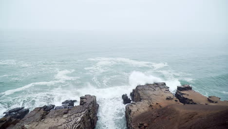 Static-shot-of-roaring-waves-hitting-the-cliffs-off-the-coast-of-Mirador-Miguel-Grau,-Chorrillos,-Lima,-Peru-during-a-cloudy-morning