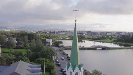 Cross-on-pointy-tower-of-Free-Church-in-Reykjavik,-Iceland,-lake-Tjörnin