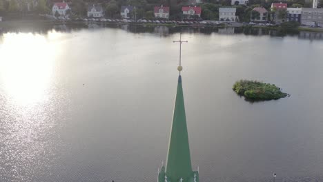 Cross-on-top-of-Bell-Tower-of-Free-Church,-Fríkirkjan-í-Reykjavík,-water-of-lake-Tjörnin