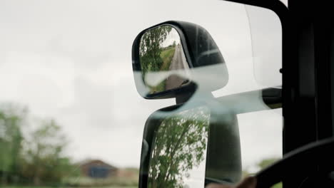 Close-up-mirror-glass-reflection-reflective-open-fields-side-viewing-angle-truck-bus-driver-driving-fast-landscape-travelling-travel-visiting-destination-looking-back-seat-belt-road-street-highway