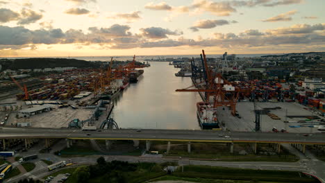 Luftaufnahme-Des-Frachtterminals-Gdynia-Bei-Sonnenuntergang,-Industriehafen-Mit-Containern,-Lastwagen,-Kränen-Und-Frachtschiffen