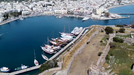Cinematic-circular-aerial-shot-of-harbor-and-castle-ruins-in-greek-island-during-sunny-day