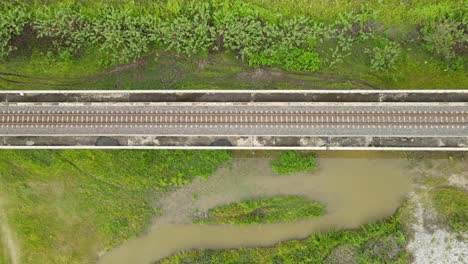 Descending-aerial-footage-revealing-the-elevated-railway,-marshland-with-green-grass-and-brown-water-from-heavy-rain-in-Muak-Klek,-Saraburi,-Thailand