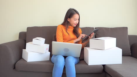 Asiatische-Frau,-Kleine-Online-Unternehmerin,-Überprüfung-Von-Bestellungen-Und-Inventar-Auf-Tablet-Und-Laptop,-Vollbild
