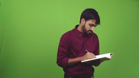 Attractive-male-student-writing-something-down-and-looking-to-someone,-isolated-on-green-screen