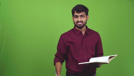 Attractive-man-Indian-teacher-holding-pen-and-book-and-pointing-to-someone,-isolated-on-green-screen