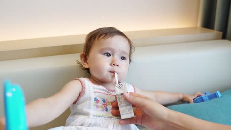 Mama-Hilft-Süßem-Asiatischem-Kleinkind,-Saft-Durch-Einen-Strohhalm-Zu-Trinken,-Während-Das-Kind-Spielt