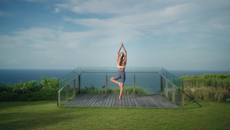 Fit-young-blond-woman-doing-tree-pose-on-cliff-viewing-platform,-Bali