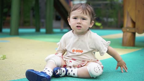 Toddler-Asian-girl-playing-on-the-playground-but-looking-bored---adorable-child-wearing-knee-pads