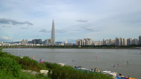 People-enjoying-the-recreational-Hangang-river---windsurfing,-paddle-boarding-and-kayaking-with-the-Seoul-city-skyline-in-the-background,-Lotter-World-Tower