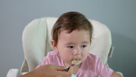 Cute-Toddler-Girl-Eating-Oatmeal-Seated-In-High-Chair-At-Home