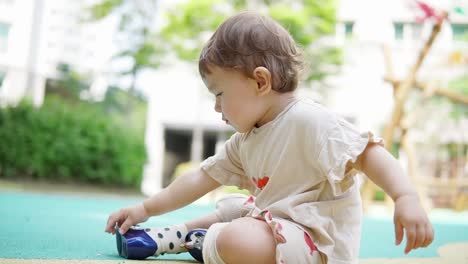 Asian-toddler-girl-sitting-on-the-playground-and-putting-things-in-her-mouth---concept:-learning,-motor-skills,-taste-,trying,-growing,-development