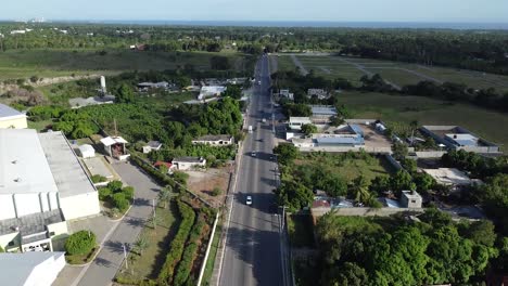 aerial-view-of-drone-focusing-from-bottom-to-top-long-road-of-bani-in-dominican-republic,-beautiful-mountains-in-background,-concept-travels-out-of-town
