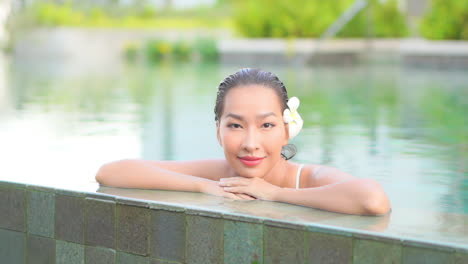 Nahaufnahme-Einer-Exotischen-Frau-Mit-Nassem-Haar-Und-Einer-Blume-Hinter-Ihrem-Linken-Ohr,-Die-Sich-Am-Rand-Eines-Resort-Swimmingpools-Lehnt