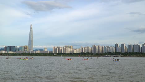 People-kayaking-and-paddle-boarding-in-Han-river-in-Seoul,-South-Korea-with-the-Lotte-World-Tower-dominating-the-city-skyline