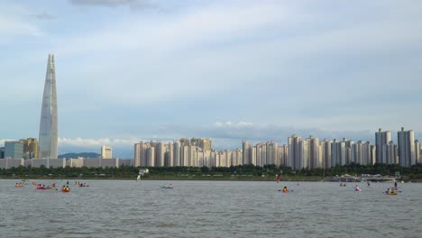 People-Group-Kayaking,-and-Windsurfing-at-Han-River-with-famous-Seoul-Landmark-Lotte-Tower-on-Background-at-sunset