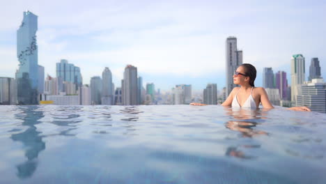 Exotic-Woman-in-Infinity-Rooftop-Swimming-Pool-With-Amazing-View-of-Modern-City-in-Background,-Full-Frame