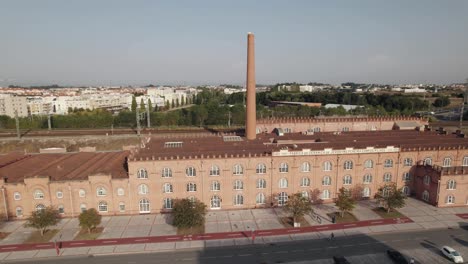 Old-factory-building-with-high-chimney-and-cityscape-of-Aveiro-in-horizon,-ascend-drone-view