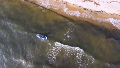 Top-down-clip-of-a-SUP-surfboard-on-the-waves-next-to-a-beautiful-tropical-beach