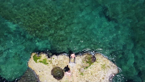 Aerial-shot-above-two-people-climbing-into-clear,-tropical-water