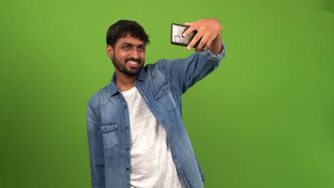 Young-Asian-man-with-well-trimmed-beard-and-mustache-taking-selfie-in-front-of-green-screen