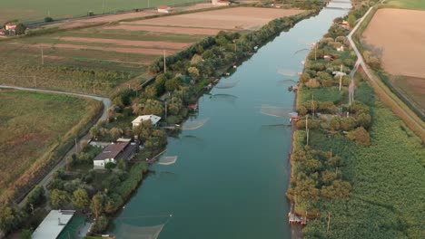 Aerial-shot-of-fishing-huts-on-river-with-typical-italian-fishing-machine,-called-"trabucco",Lido-di-Dante,-fiumi-uniti-Ravenna-near-Comacchio-valley