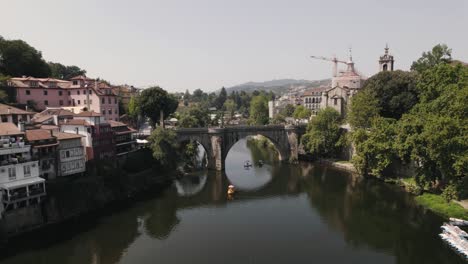 Medieval-bridge-of-Amarante-town-with-cityscape-and-river-water,-aerial-flying-forward-view