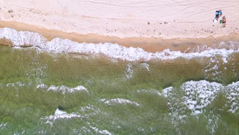 Slow-motion-overhead-drone-clip-over-a-beatiful-beach-with-crystal-waters-and-waves-crushing-on-the-ground-in-Keramoti,-Kavala,Northern-Greece