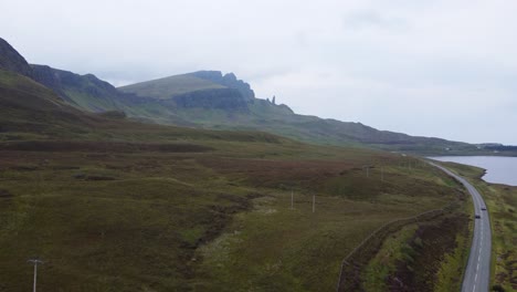 Car-driving-along-road-leading-to-Old-Man-of-Storr,-Famous-Landmark-on-Isle-of-Skye,-West-Coast-of-Scotland---Aerial-Drone-4K-HD-Footage-Rise-Up