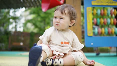 Curious-Baby-Girl-With-Knee-Pads-Sitting-And-Playing-In-An-Outdoor-Playground