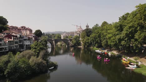 Amarante-town-skyline-with-ancient-stone-bridge-and-many-modern-animal-boats-in-river-water,-aerial-view