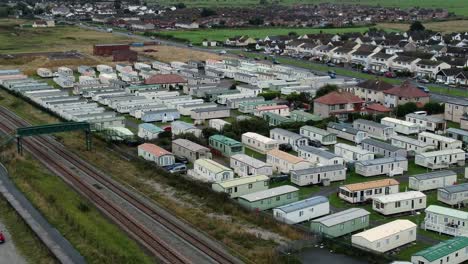 Static-caravan-trailer-beachfront-staycation-holiday-home-campground-resort-aerial-descending-view-above-railway-tracks