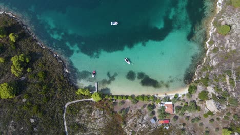 Overhead-drone-clip-of-a-small-tropical-island-bay-with-crystal-blue-water-and-luxurious-boats-in-the-area-of-Vourvourou,-in-Northern-Greecem-Halkidiki-in-4K