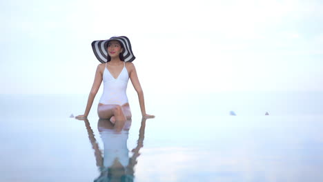 Rule-of-thirds-A-beautiful-young-woman-in-a-white-one-piece-swimming-suit-and-floppy-straw-hat-is-on-the-edge-of-an-infinity-edge-swimming-pool