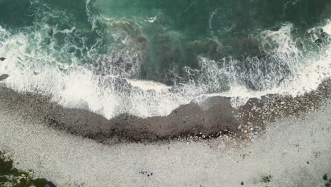 4K-footage-of-a-drone-flying-over-the-waves-hitting-the-beach,-staying-still