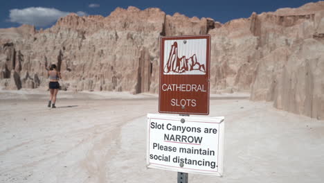 Signs-at-Cathedral-Gorge-State-Park-ion-Plateau-n-Front-of-Narrow-Slots-Canyons-and-Female-Visitor-Passing-By,-Close-Up