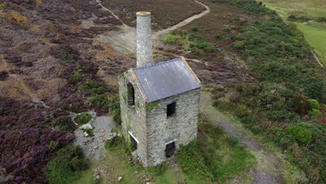 Parys-mountain-abandoned-brick-chimney-copper-mining-mill-stone-ruin-aerial-view-left-top-down-rotation