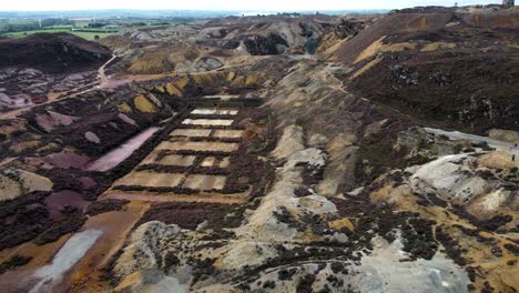 Parys-mountain-abandoned-historic-copper-mine-red-stone-mining-industry-landscape-aerial-view-descending-birdseye