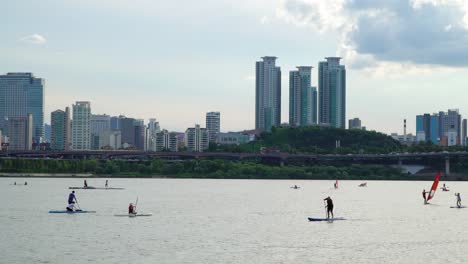 Locals-And-Tourists-Paddle-Boarding-On-Han-River-With-Asem-Tower-At-Background-In-Seoul,-South-Korea