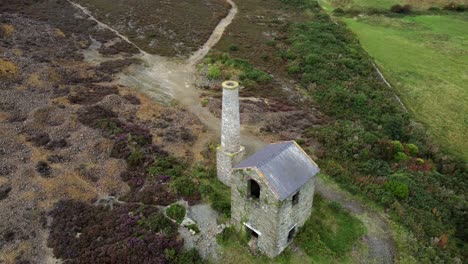 Parys-mountain-abandoned-brick-chimney-copper-mining-mill-stone-ruin-aerial-view-descending-birdseye