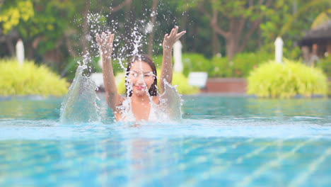 Smiling-Asian-girl-splashes-water-with-hands-in-pool