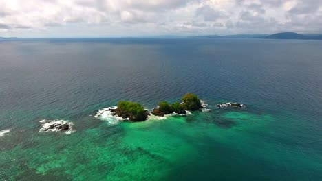 Rising-Aerial-View-Over-Small-Coral-Islands-with-Clear-Water-and-Surrounding-Waves