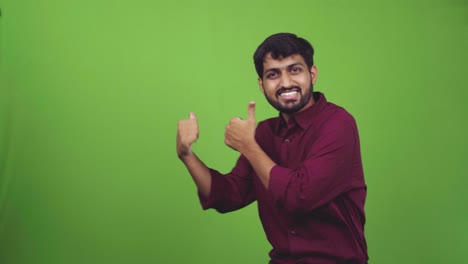 Attractive-young-man-showing-something-behind-him-with-thumbs,-isolated-on-green-screen