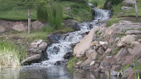 Water-rapidly-flowing-from-small-cascade-waterfall-into-pond-in-park