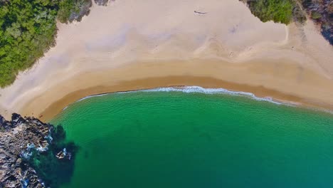 Ascending-Overhead-View-of-Clear-Emerald-Waves-Lapping-an-Empty-White-Sand-Beach-Cove