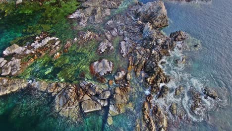 Overhead-Hover-View-of-Dramatic-Detailed-Rock-Formations-with-Ocean-Waves-Crashing